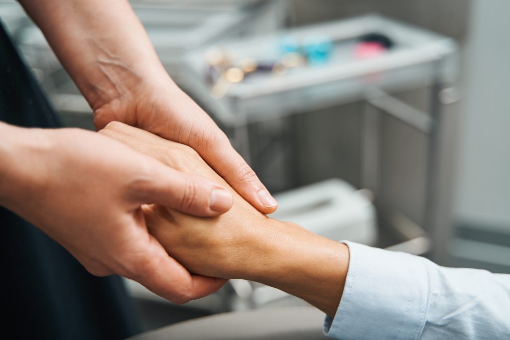Close-up of one person gently holding another’s hand, offering comfort and support in a calm, indoor setting—reflecting the compassionate approach of Heidelberger Integrative holistic care.
