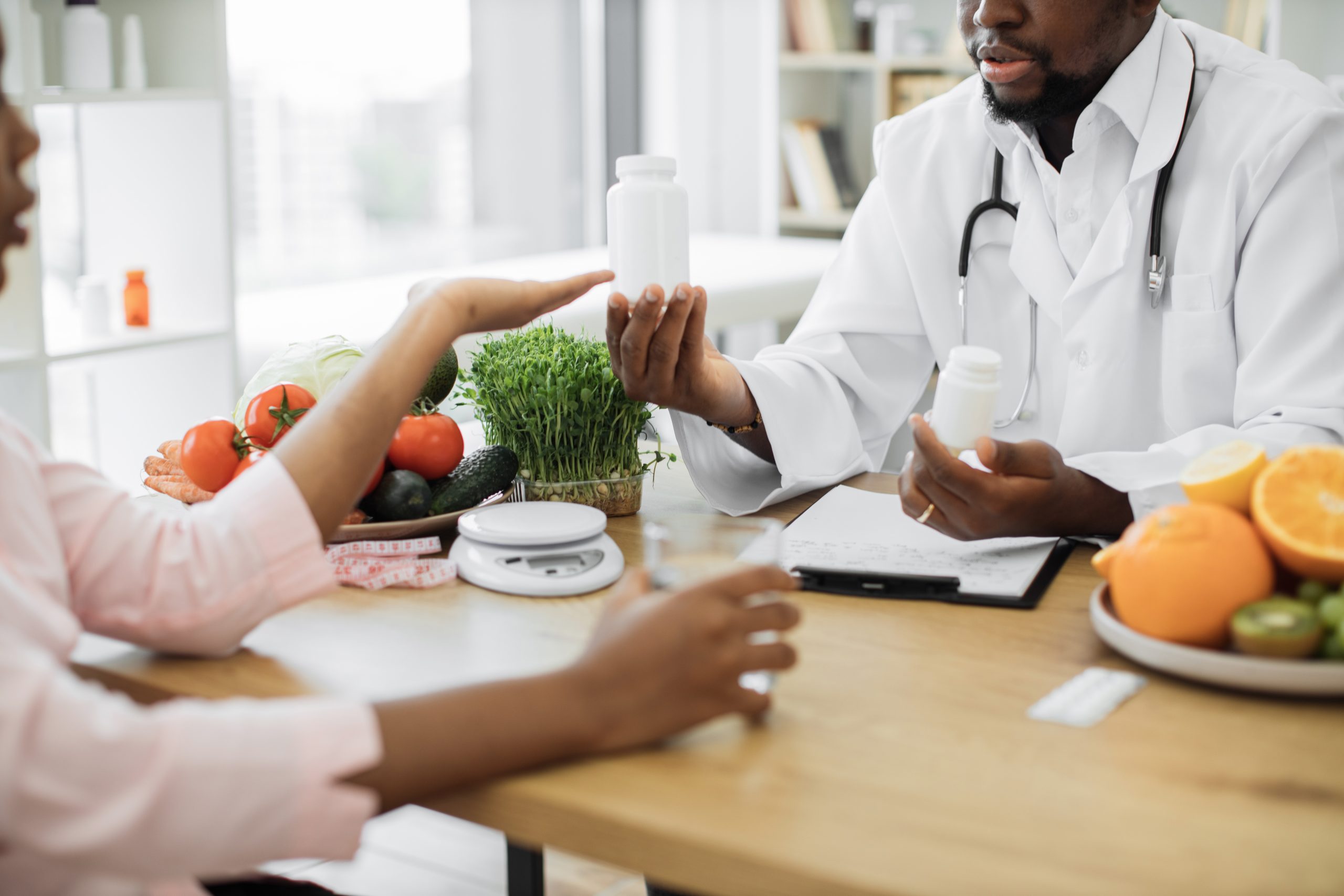 A doctor discusses medication with a patient at a table covered with fresh fruits, vegetables, and supplements, emphasizing nutrition, wellness, and health.