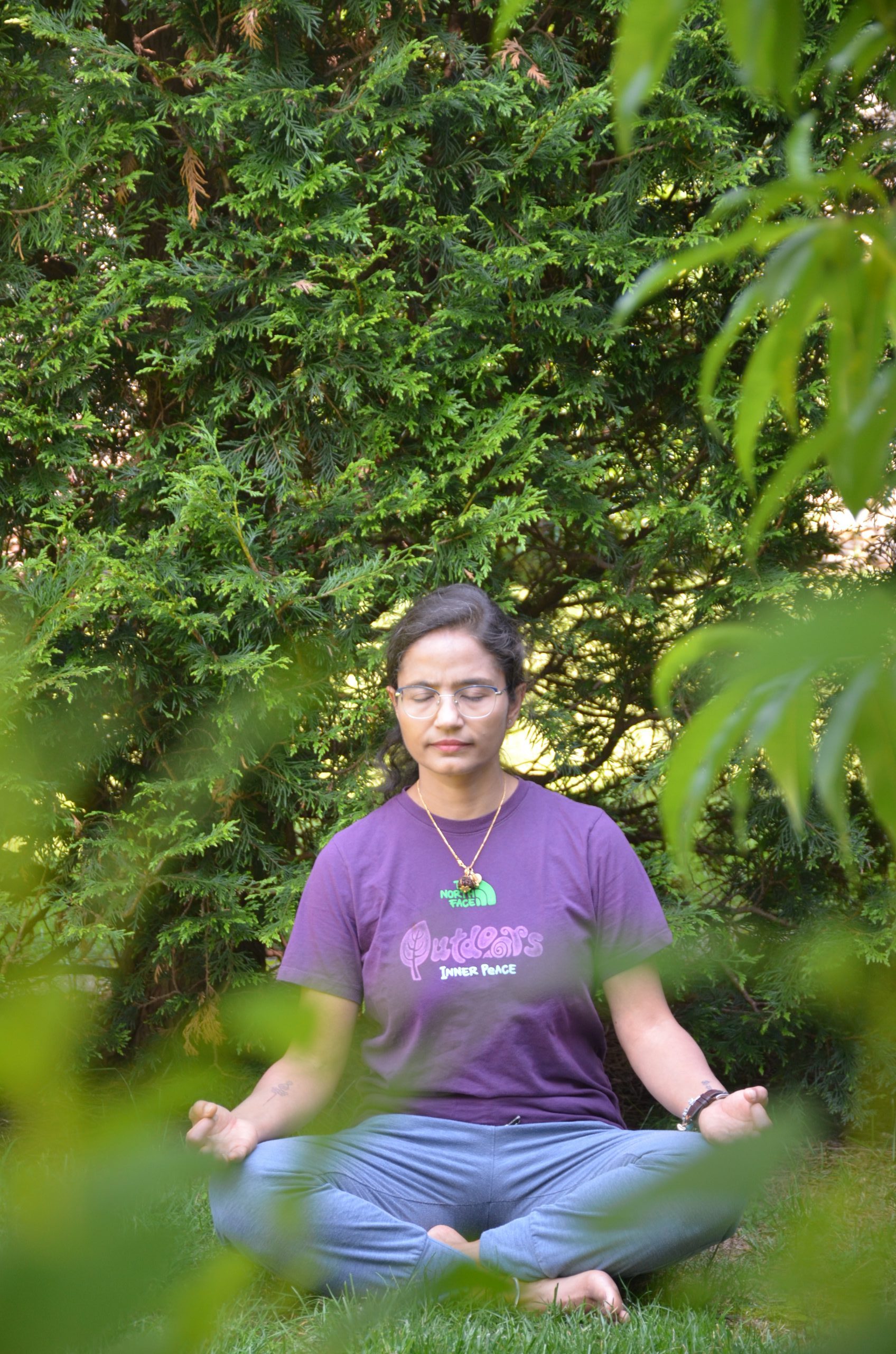 A person sits cross-legged on grass, meditating with eyes closed and hands resting on knees, surrounded by lush greenery—a peaceful scene reflecting holistic care and the principles of Heidelberger Integrative wellbeing.